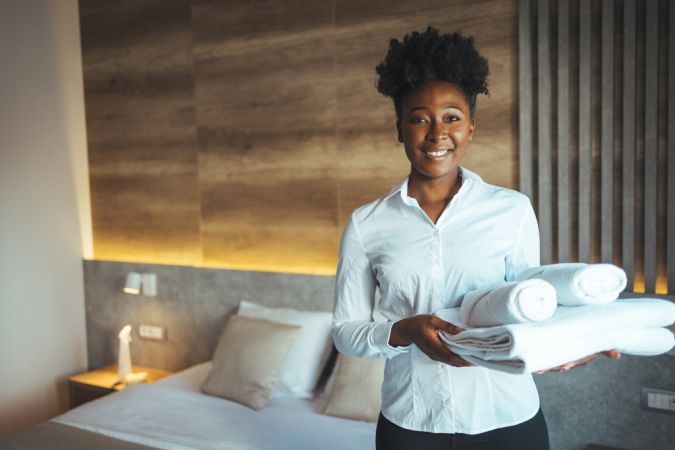 Hotel,Staff,Setting,Up,Pillow,On,Bed.,African,Housekeeper,Looking